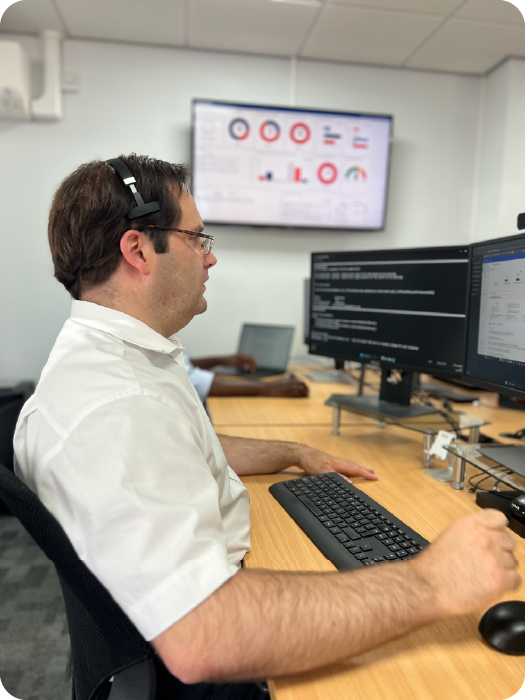 Person sitting at a desk with multiple computer monitors in an office setting providing remote IT support to customers.