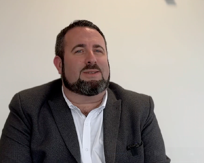 Man wearing a gray suit and white shirt against a plain background