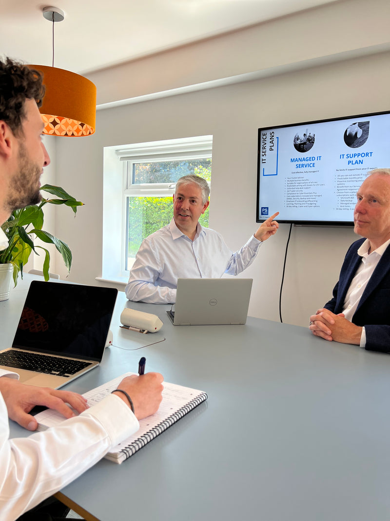 Three people in a room with a computer screen reviewing managed IT services.