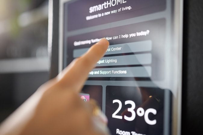 Person interacting with a smart home control panel displaying room temperature.