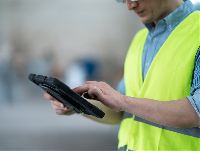 Person wearing a high-visibility vest using a tablet device.