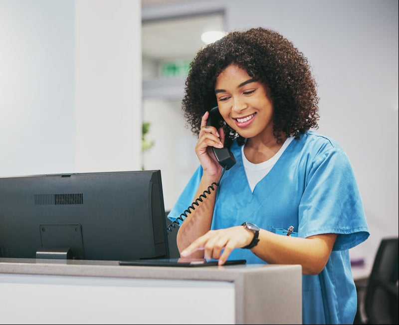 Woman in a carers uniform using a computer and phone in an office setting