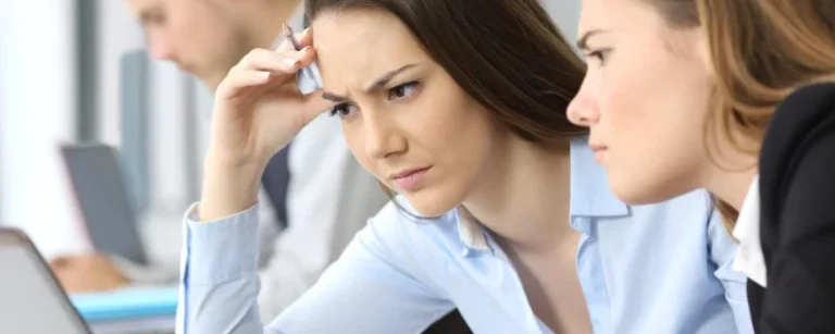2 people looking at a laptop in an office looking confused at a problem on their computer.