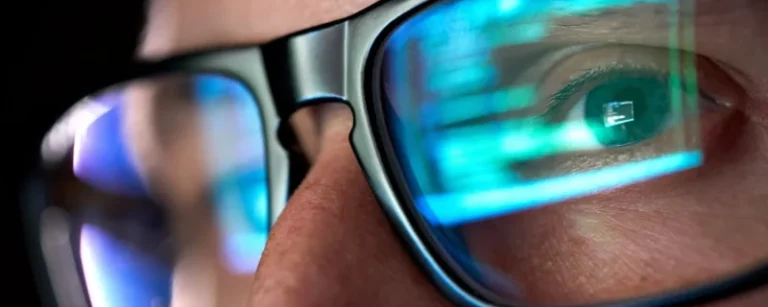 Close up of someone wearing glasses with a reflection in the lenses of a computer screen.